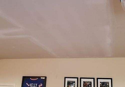 Beige wall and ceiling with framed photos and a dark sign near the top edge
