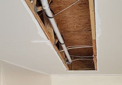 Ceiling with a rectangular opening exposing wooden framing and a white pipe during renovation