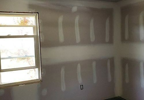Empty drywall room with taped seams and a window letting in daylight.