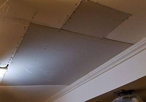 Ceiling with large, unevenly patched drywall panels and visible screws near a white crown molding edge
