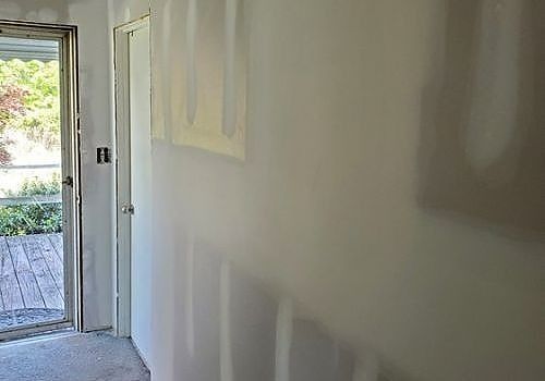 Partially finished hallway with drywall patches, open door to a bright outdoor deck on the left