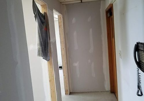 Narrow hallway under renovation with unfinished drywall, a hanging plastic sheet, and a wall-mounted phone/intercom.