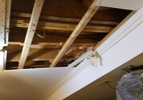 Damaged ceiling with exposed wooden beams and a hanging white drywall section
