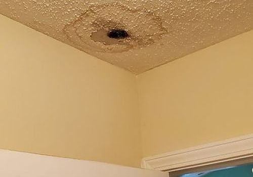 Water stain and dark hole on a beige ceiling corner above a doorway