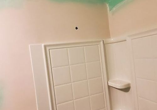 White tiled shower stall with a built-in shelf in a pale pink bathroom