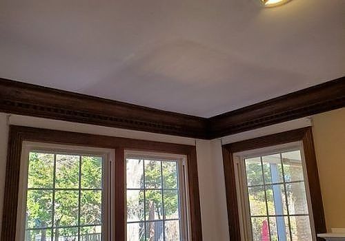 Sunlit room corner with wood crown molding and large windows looking out to trees