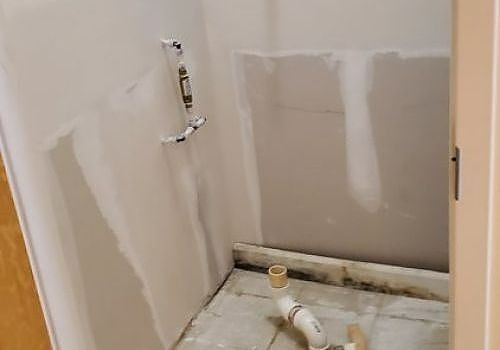 Partially finished bathroom wall with patchy drywall and exposed plumbing pipe.
