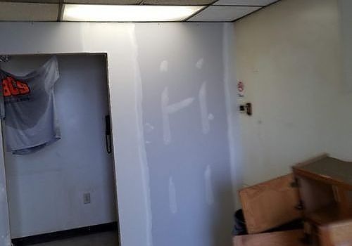 Empty room with unfinished white wall, fluorescent ceiling lights, and a T-shirt hanging in a doorway.
