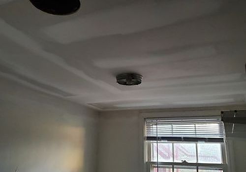 Ceiling with a central light fixture above a window with blinds in a plain room