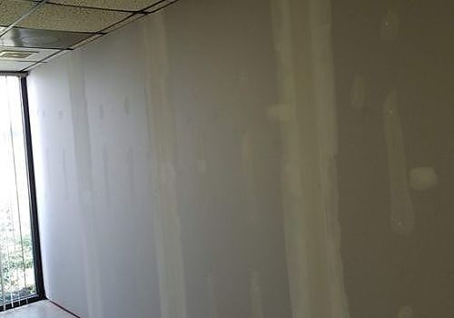 Interior wall under renovation with drywall seams and patching compound near a ceiling corner
