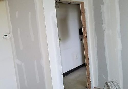 Partially finished hallway with white drywall, a doorway, and bare wooden trim