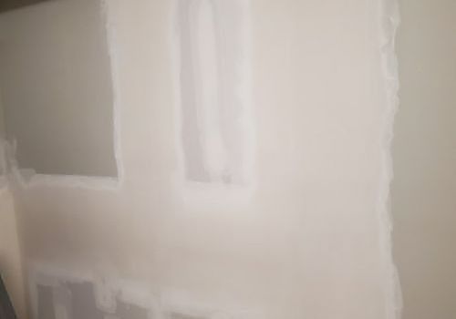 Pale unfinished drywall with taped seams and patch marks inside a room.