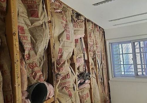 Room under renovation with floral wallpaper stripped back to exposed wall and a window at right