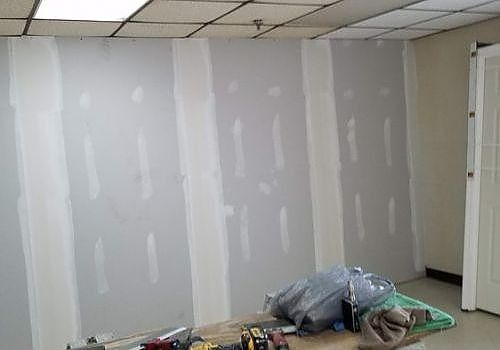 Partially finished room with drywall, ceiling tiles, and construction materials on the floor