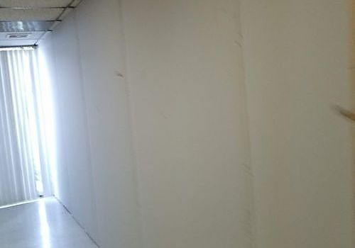 Narrow white hallway with a bright doorway at the end and vertical blinds on the left