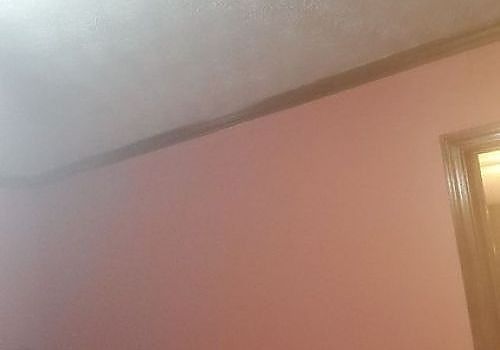Pink wall and ceiling corner with a wooden doorframe on the right.