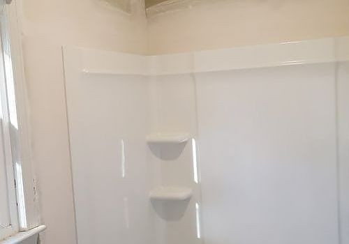 White shower/tub surround with built-in corner shelves and a window on the left