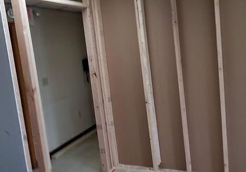 Narrow hallway under construction with exposed wall studs and an open doorway to a tiled room