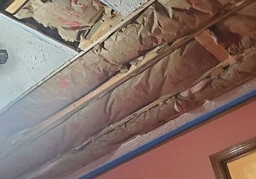 Damaged ceiling insulation exposed above a pink wall with blue trim