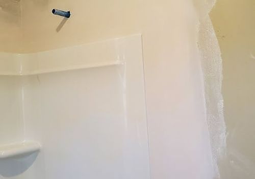 Partially tiled bathroom wall with a shower niche and a loose blue fixture near the top