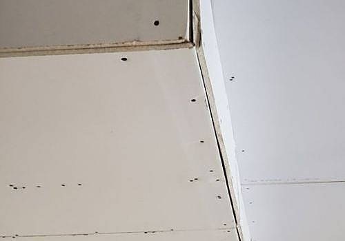 Close-up of a wall and ceiling corner with visible seams and screw holes.