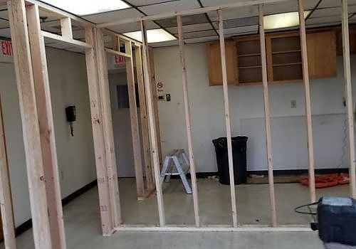 Partially framed room with exposed wall studs, open cabinets, and scattered renovation materials