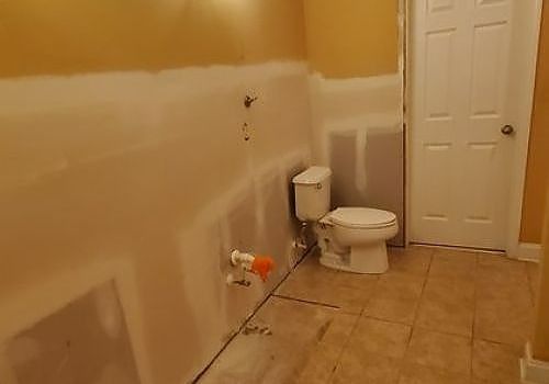 Partially renovated bathroom with tiled floor, white toilet, and unfinished walls with exposed plumbing