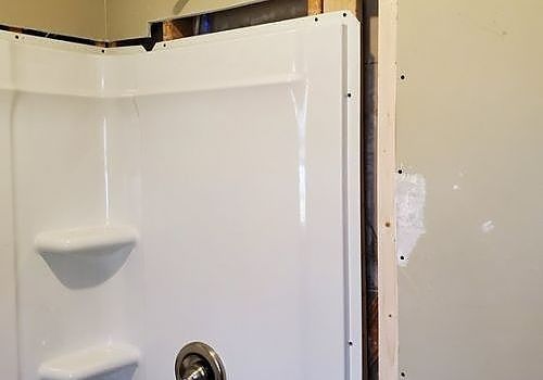 White shower stall door partly open against a beige bathroom wall.