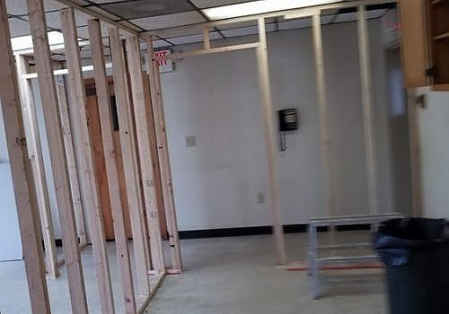 Unfinished interior with exposed wall studs, white walls, and a gray trash bin near the right side.