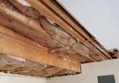 Exposed ceiling joists and insulation in a damaged ceiling, with a section missing near the wall