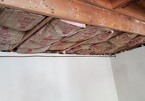 Exposed ceiling insulation above a white wall corner with wooden beams visible