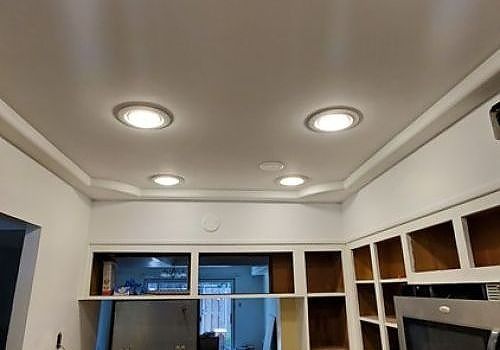 White kitchen ceiling with recessed lights above open cabinets and a window.