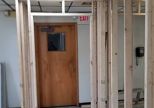 Interior construction site with wooden framing and a closed door under an EXIT sign.