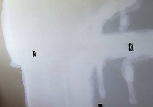 Unfinished drywall with taped seams, patchwork, and electrical outlets in a room under renovation