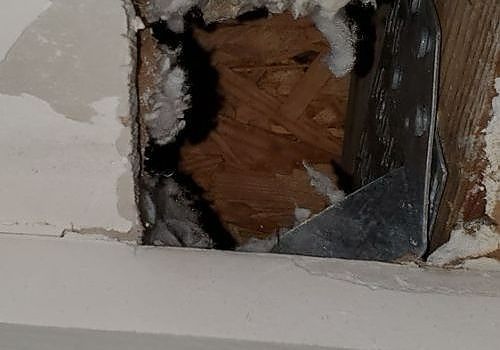 Damaged wall with a rectangular hole exposing wood and insulation.