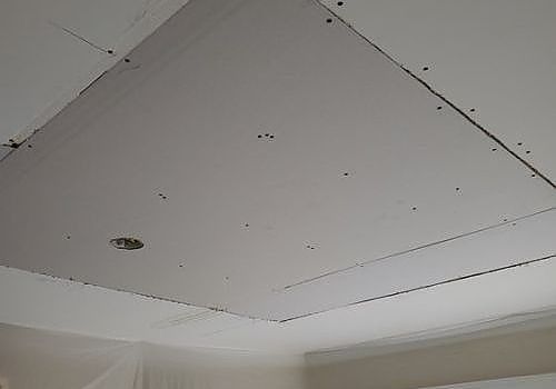 White ceiling with a recessed access panel and a small hole or fixture opening in the corner of a room