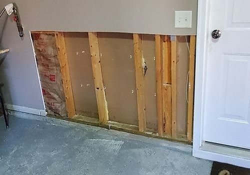 Wall section with drywall removed, exposing wooden studs beside a white door.