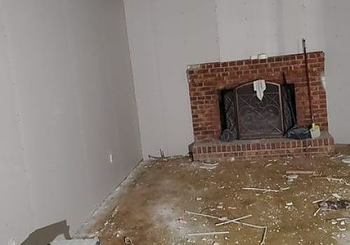 Small room corner with a brick fireplace and debris scattered on the floor.