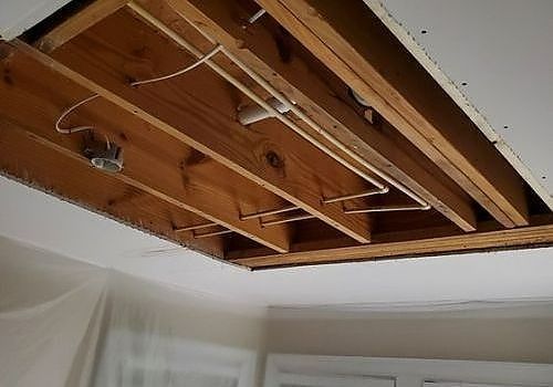 Exposed ceiling joists and wiring in a room with a section of drywall missing