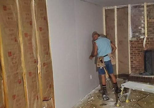 Worker using power tools to strip drywall in a room under renovation
