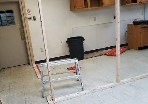Empty room with ladder, trash can, and kitchen cabinet near a doorway