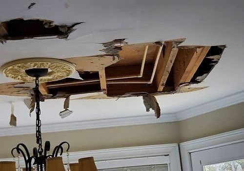 Damaged ceiling with exposed wooden beams and hanging chandelier in a room