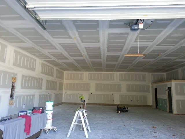 Large unfinished garage interior with drywall, a ladder, workbench, and tools on the floor.
