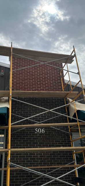 A yellow scaffolding is sitting in front of a brick building.