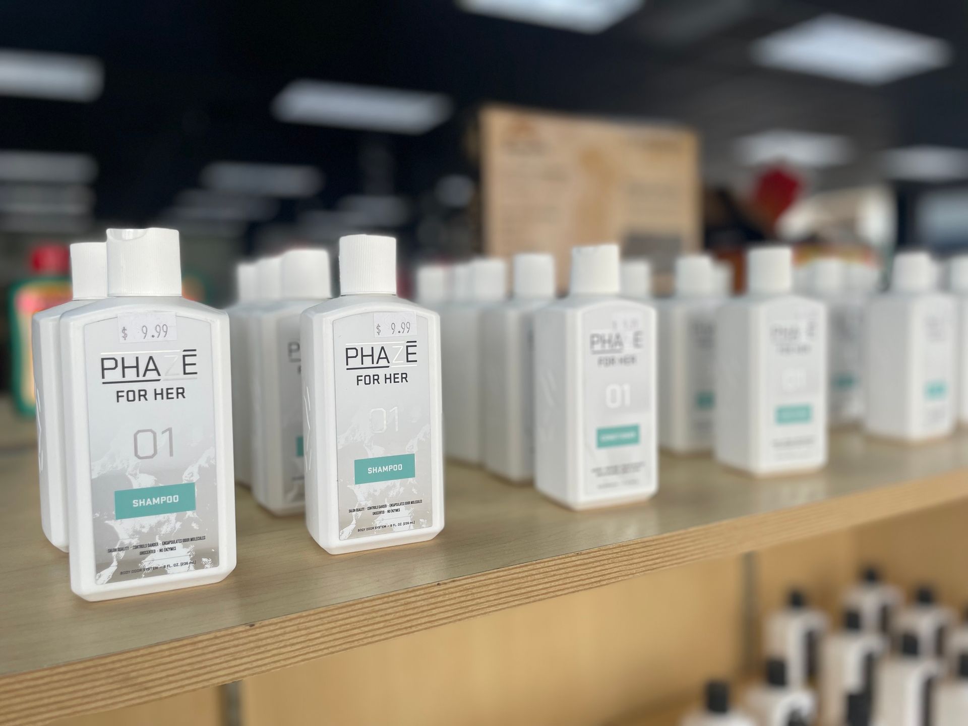 Bottles of PHA+E skincare products on a shelf, white with black text and turquoise accents.