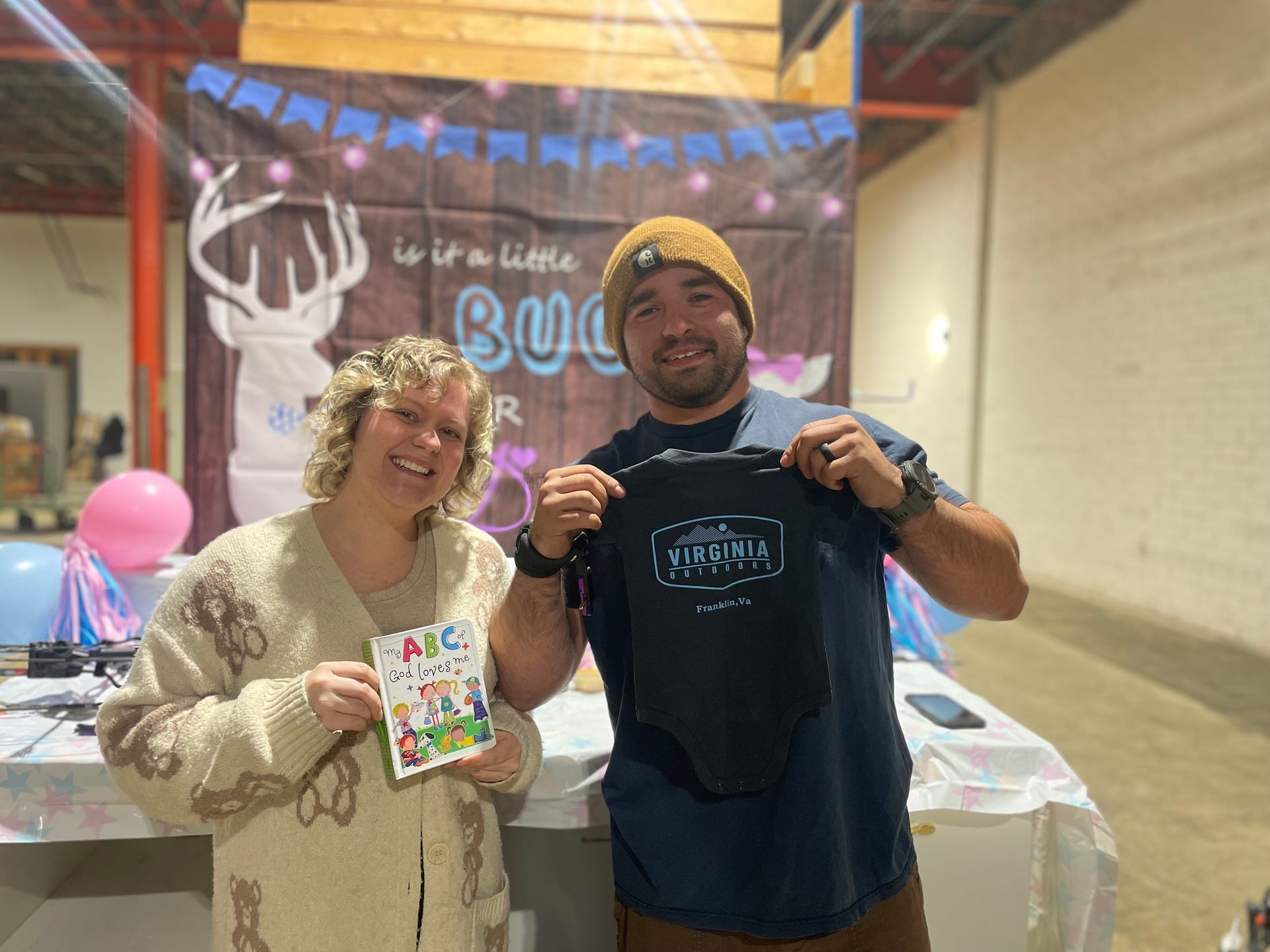 Two smiling people holding up event items at a table with a “BOO” Halloween-themed backdrop