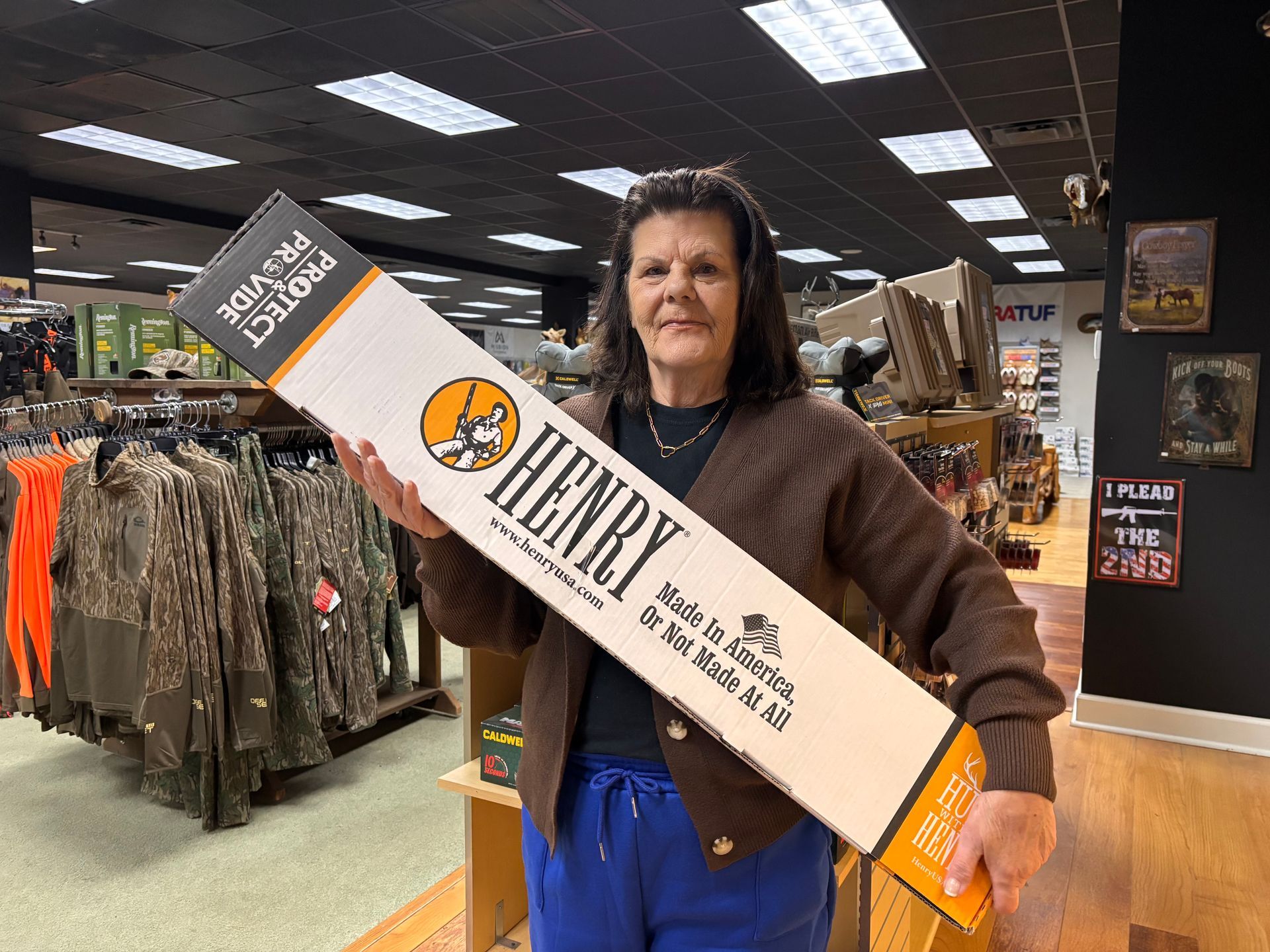 Woman holding a long box with HENRY written on it inside a store with clothing racks.