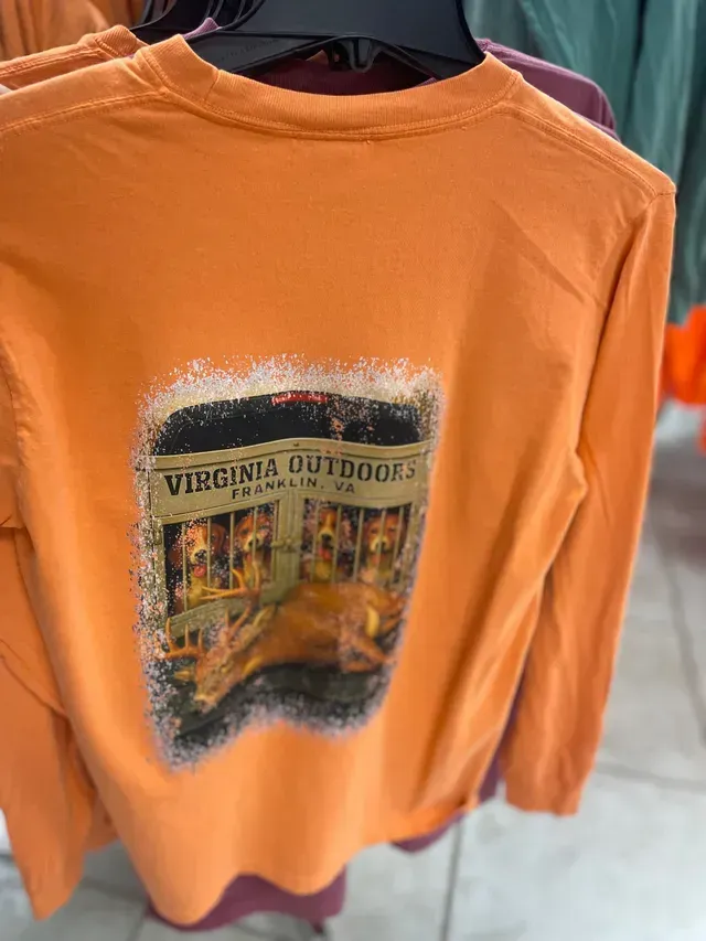 Orange long-sleeve shirt with a Virginia Outdoors graphic hanging on a clothing rack