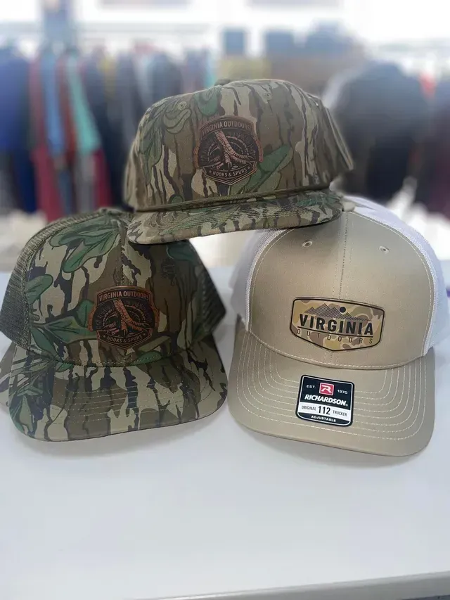 Three Virginia baseball caps: two camouflage and one tan, displayed on a white surface.