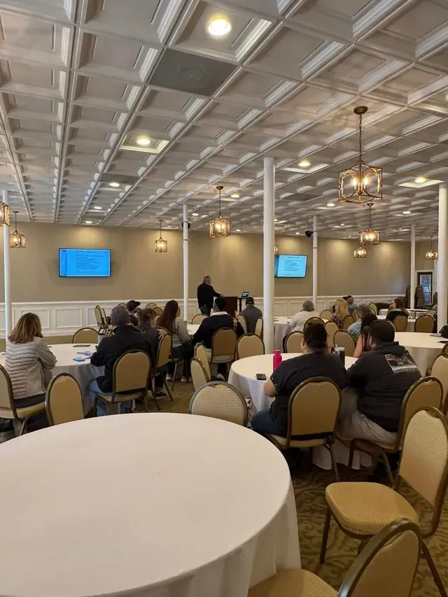 Conference room with seated attendees facing a presentation screen in a formal banquet hall